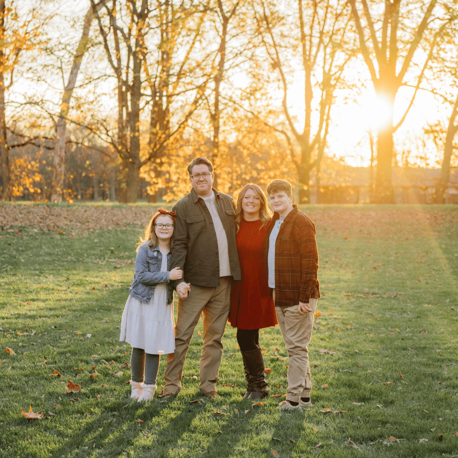 photo of a family. 1 man, 1 woman, 1 son, and 1 daughter. Sunlight in the background shining through trees.